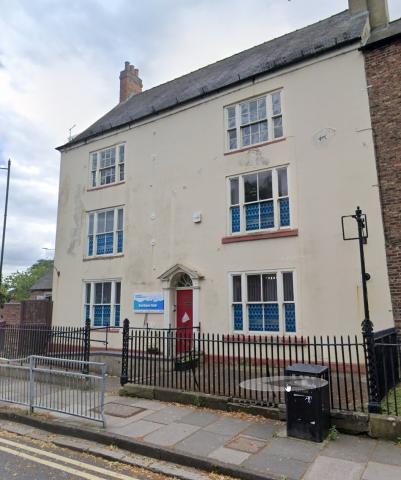 Cream building with blue and white sign and a red door. Three floors with an entrance to the side with buzer.